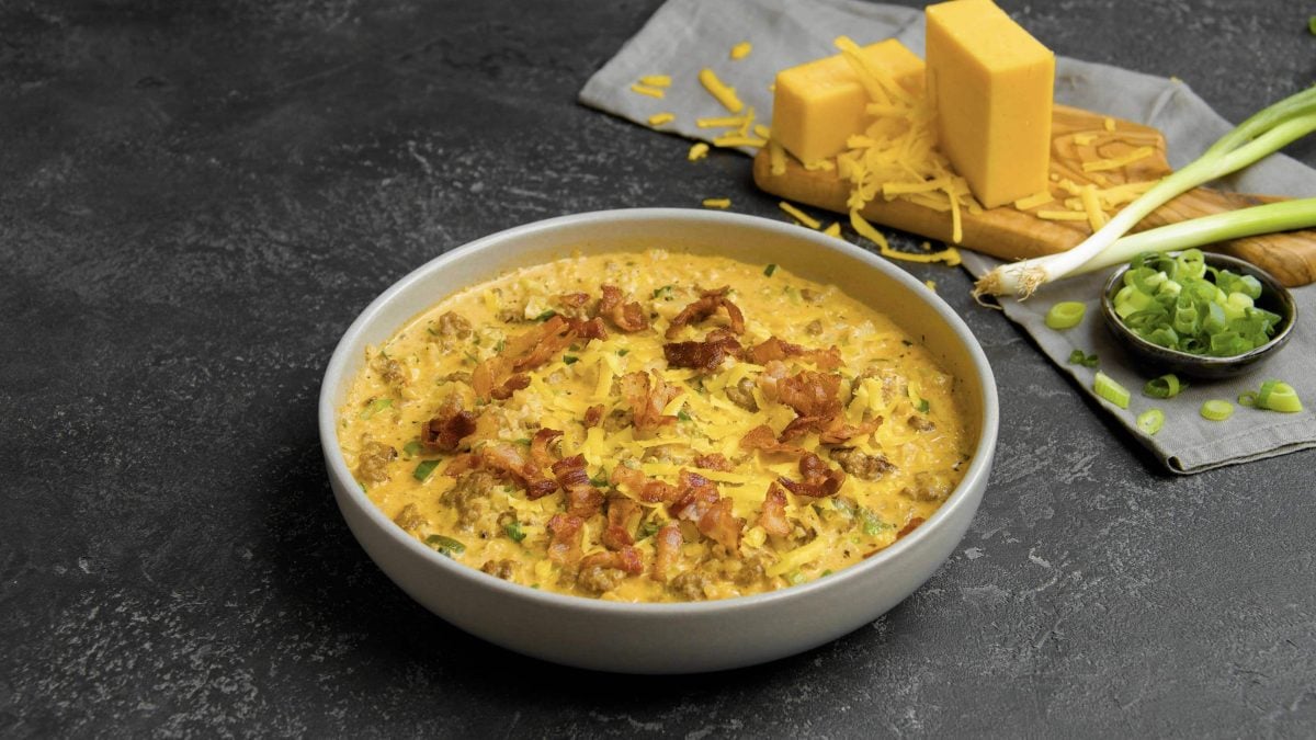 Die Low-Carb-Cheeseburger-Pfanne angerichtet in einem weißen Teller. Im Hintergrund geriebener Käse und Frühlingszwiebeln.