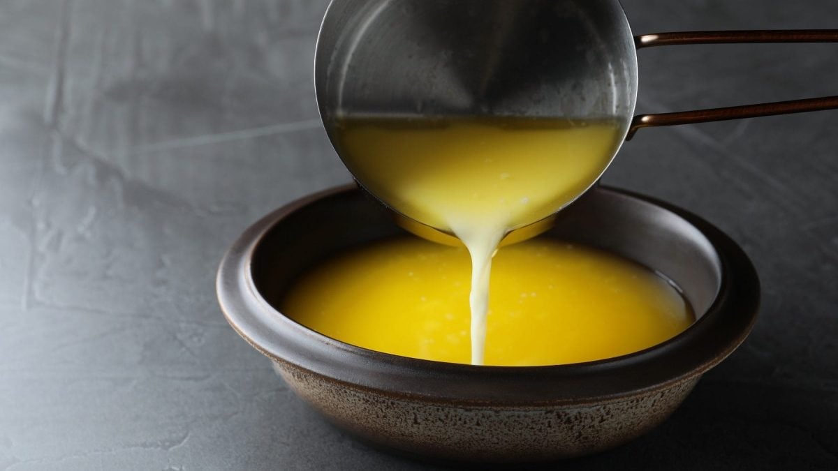 Vor einem dunklen Hintergrund ist eine SChale und ein Topf zu sehen. Aus dem Topf wird eine gelge Flüssigkeit in die Schale geschüttet. Bei der Flüssigkeit handelt es ich um geklärte Butter.