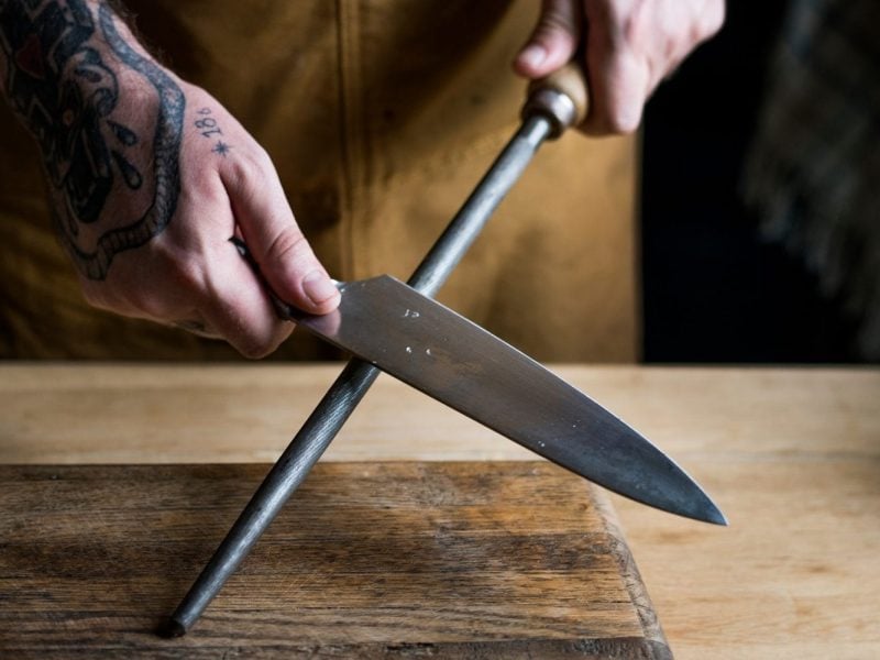 zwei Hande schärfen an einem Wetzstahl ein Küchenmesser