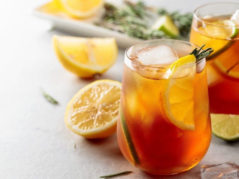 Zwei Gläser Earl Grey Gin Tonic mit Zitronenscheiben, Eis und Rosmarinzweigen. Im Hintergrund unscharf die Zutaten.