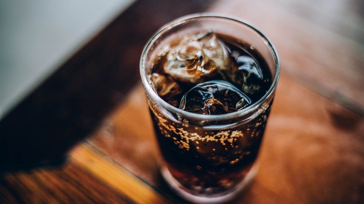 Electricity Cuba Libra mit Eiswürfeln im Highball Glas auf dunklem Holztablett. Aufnahme aus der Vogelperspektive.
