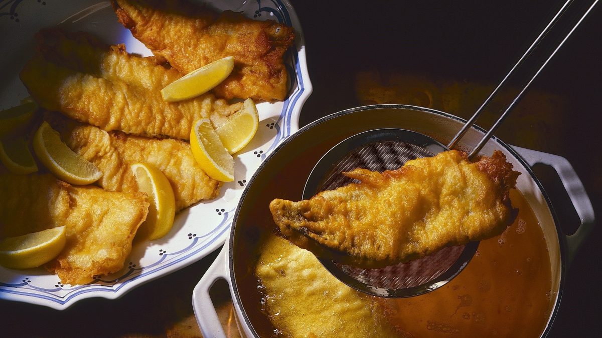 Frittierter Karpfen, aus dem Öl mit einer Schöpfkelle heraus gehoben und in einer Schale zum Abtropfen beiseite gestellt, garniert mit frischen Zitronenscheiben.