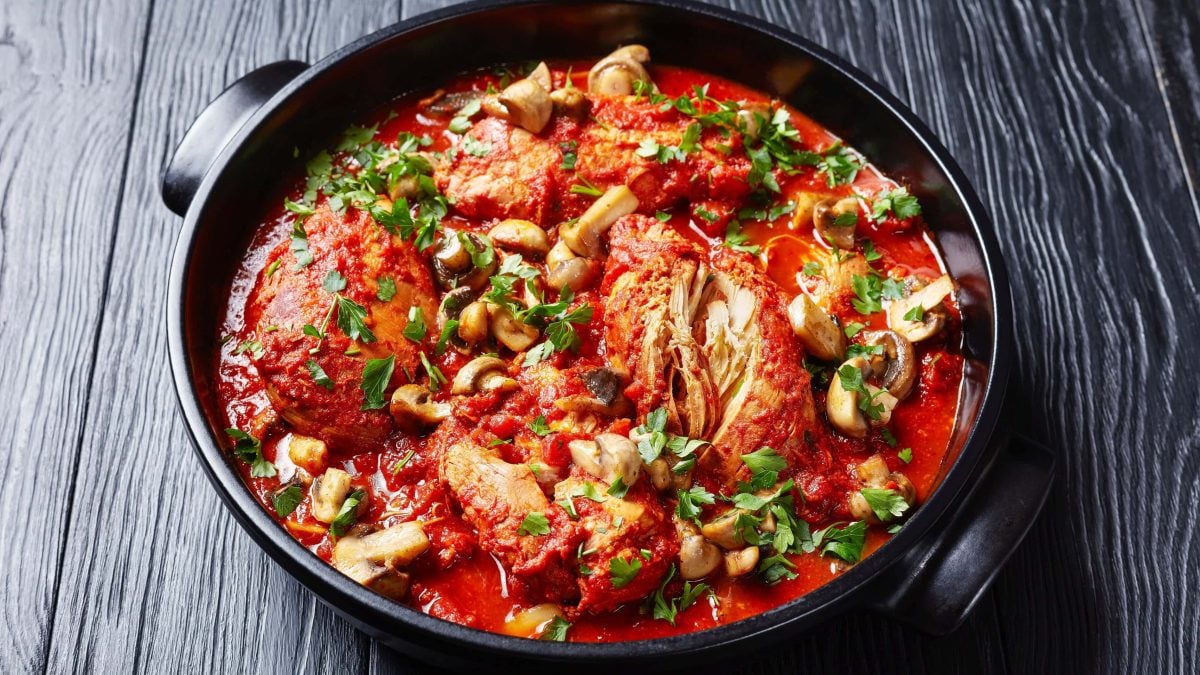 Chicken cacciatore aus Der Pate Hähnchen sizilianische Art in Gusspfanne auf Holztisch mit Petersiliengarnitur. Aufnahme aus der Draufsicht.