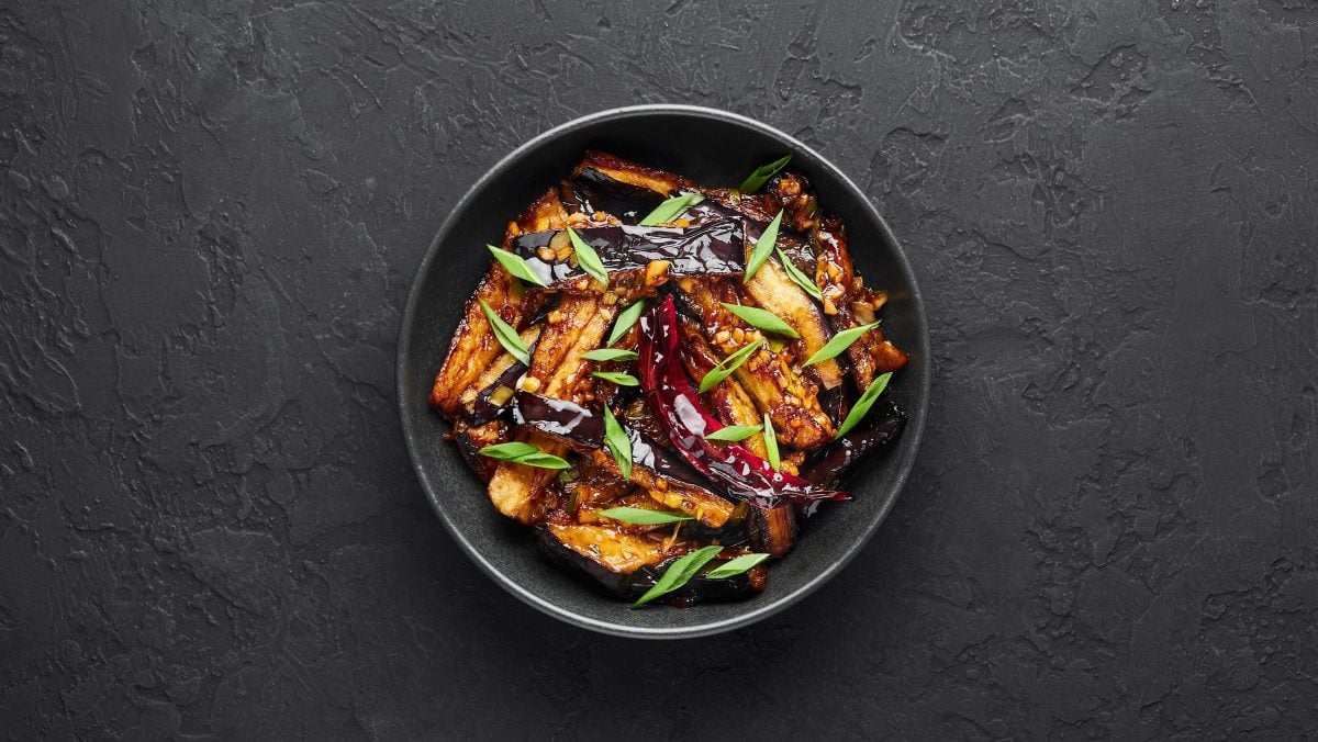 Geschmorte chinesische Aubergine mit dunkler Sauce, Erdnüssen, Limette und Chili in einer schwarzen Schale auf einer schiefer Tafel