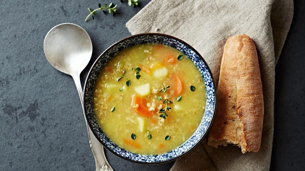 Graupen-Suppe mit Petersilienwurzel, Sellerie, Karotte und Graupen, mit Majoran garniert in einer gemusterten Schale auf einem steinernen Untergrund