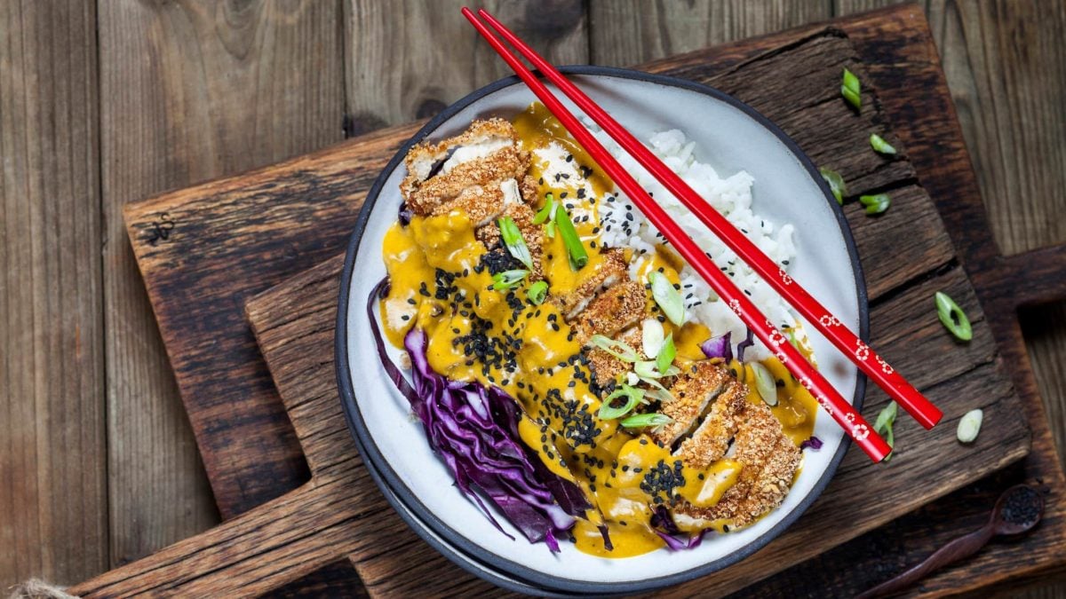Katsu Curry japansiches Curry Gericht mit Reis und Rotkohl auf weißem Teller, Holzbrettern und Holztisch. Zwei rote Essstäbchen lieben auf dem Teller. Aufnahme aus der Vogelperspektiv.