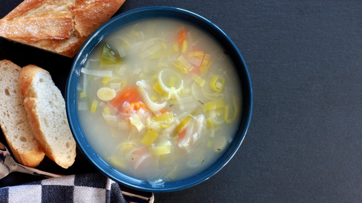 Eine Schüssel Lauchsuppe inspiriert von der Serie Emily in Paris, daneben liegt ein angeschnittenes Baguette.