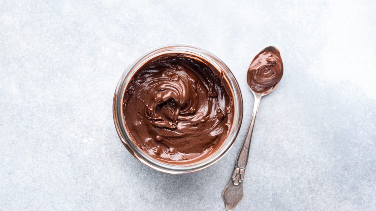 Ein Glas selbst gemachte Nutella in der Draufsicht, daneben liegt ein Teelöffel mit der Haselnusscreme.