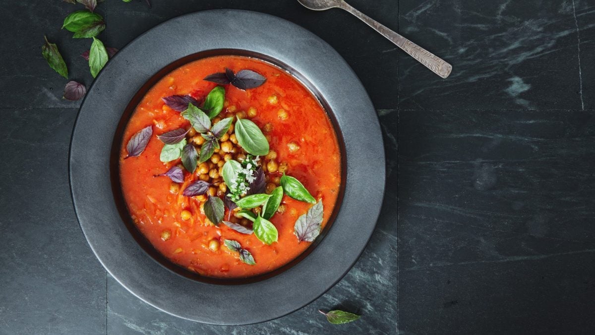 Ein Teller orientalische Tomatensuppe mit Kichererbsen sowie frischen Kräutern in der Draufsicht.