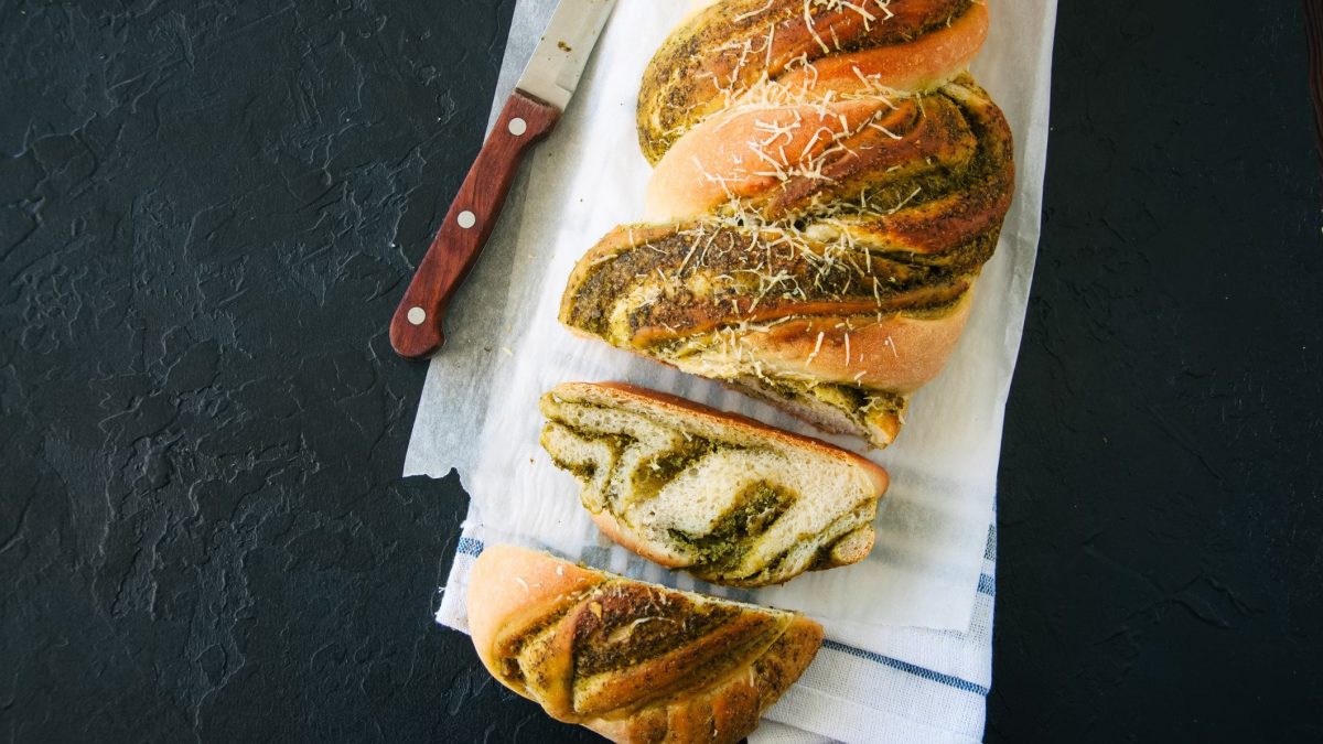 Ein angeschnittenes Pestobrot mit Quinoa in der Draufsicht. daneben liegt ein Messer.