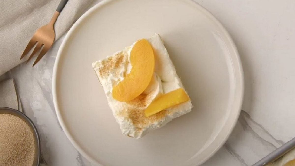 Ein Stück Pfirsich-Schmandkuchen platziert auf einem weißen Teller.