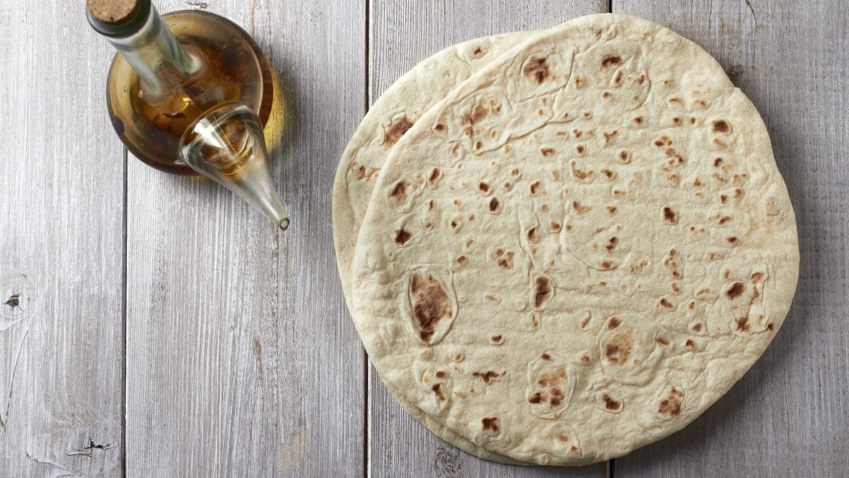 Piadina zwei Piadine Romagnola auf Holztisch. Daneben Olivenöl in einer Glaskaraffe. Aufnahme aus der Vogelperspektive.