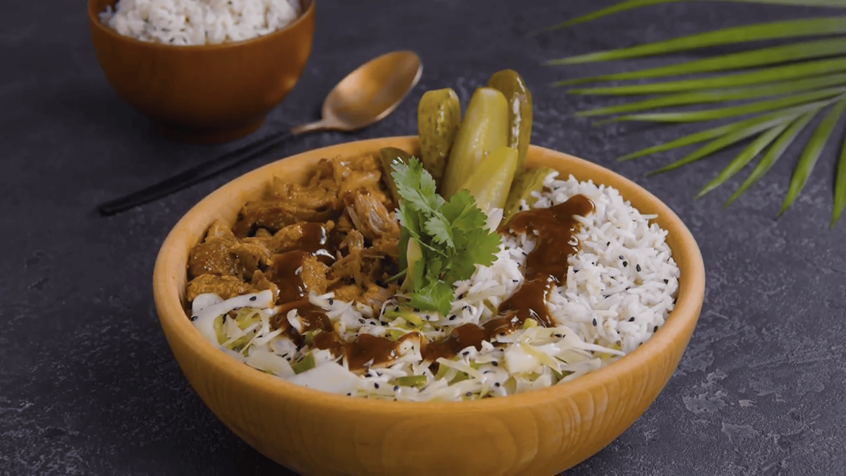 Pulled Pork Bowl mit Koriander und Barbecue-Sauce als Deko in Holzschale auf dunkelgrauem Tisch. Aufnahme aus der Draufsicht.