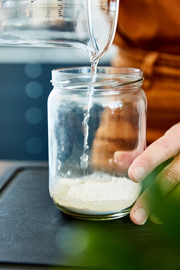 Eine Frau gießt Wasser in ein Glas mit etwas Mehl.