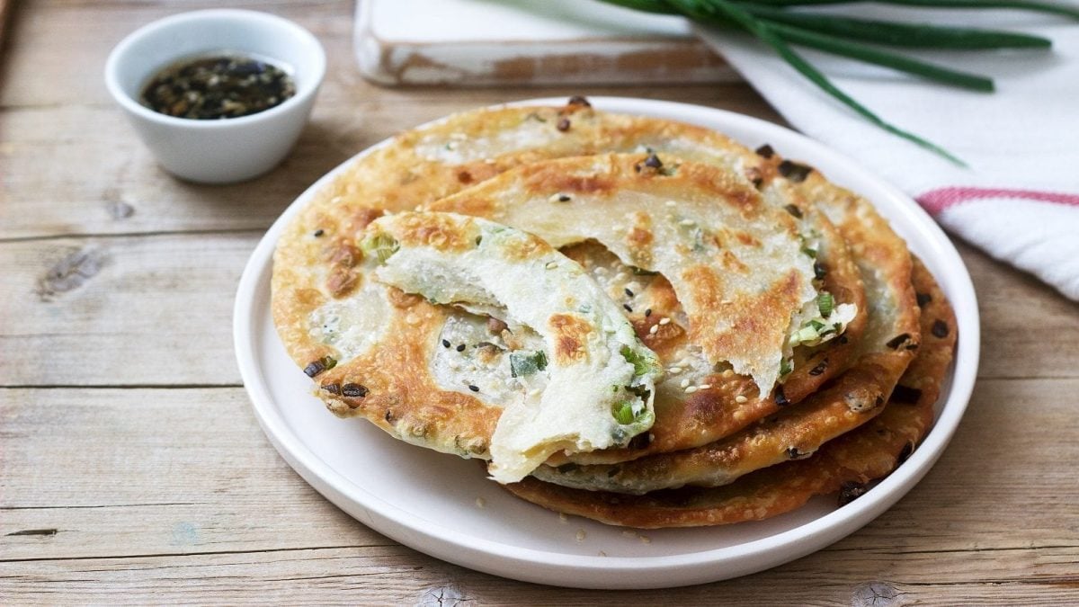 Mehrere Scallion Pancakes liegen auf einem weißen Teller und warten darauf, verzehrt zu werden.