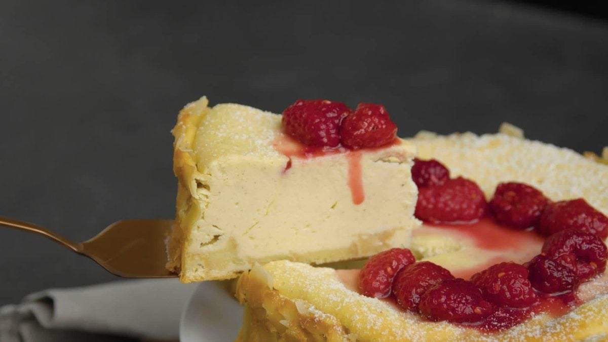 vor einem dunklen Hintergrund ist eine Für Naschkatzen: Der cremige Schüttel-Käsekuchen mit Himbeer-Sauce zu sehen, wie er gerade angeschnitten wird.