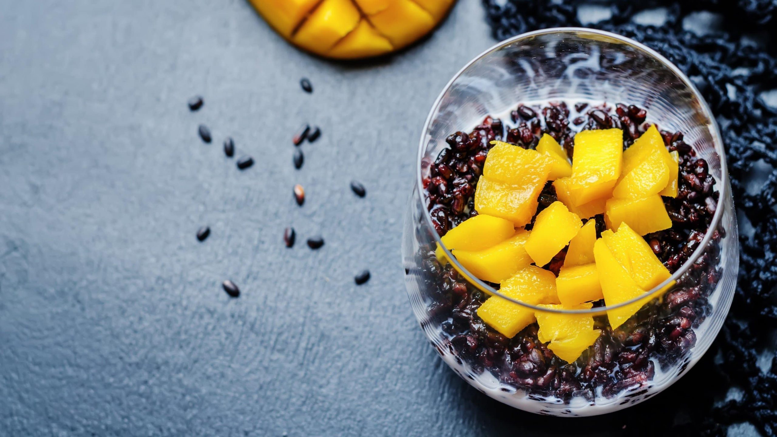 Cremiger Reispudding mit Kokosmilch und gehackter Mango in einem Glas Serviert auf grauem Hintergrund