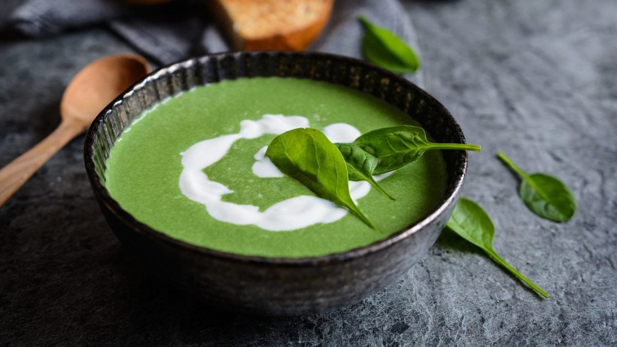 Eine Schüssel mit grüner Suppe und selbst gemachter Hafersahne sowie ein paar Basilikumblättern.