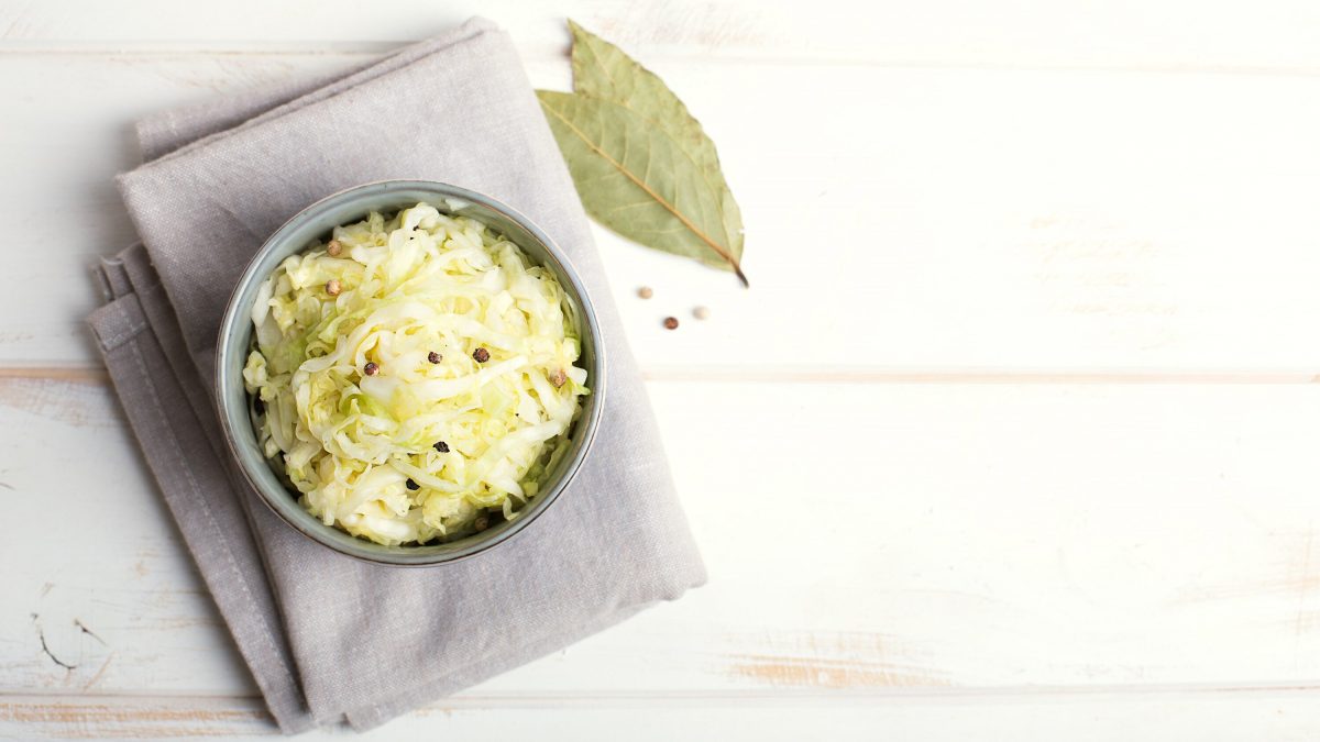 Saftiges selbst gemachtes Sauerkraut gewürzt mit Wachholderbeeren und Lorbeer, serviert in einer Schüssel auf hellem Hintergrund