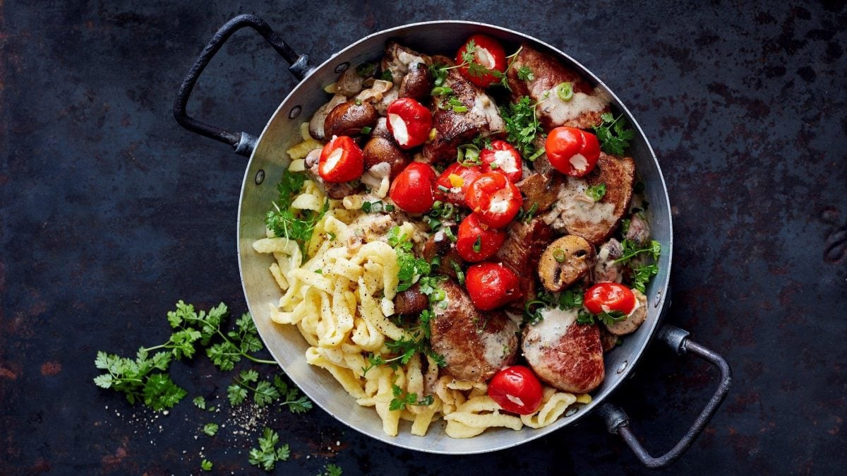 Schweinefilet, Champignons, mit Frischkäse gefüllte Kirschpaprika und natürlich Spätzle: unsere Spätzle-Jägerpfanne steht angerichtet auf einer schwarzen Platte.
