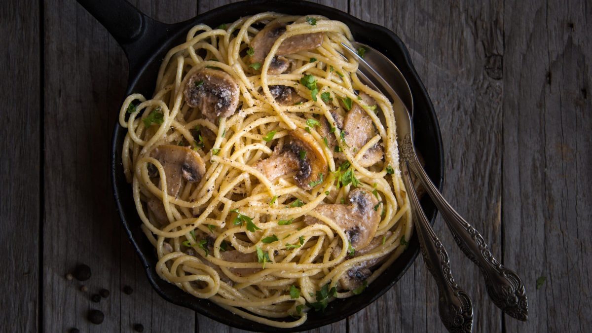 Eine Pfanne Spaghetti mit Tahinisauce, darin stecken Gabel und Löffel.