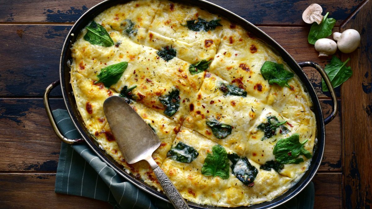 Eine ovale Form mit Spinatlasagne aus der Pfanne in der Draufsicht.