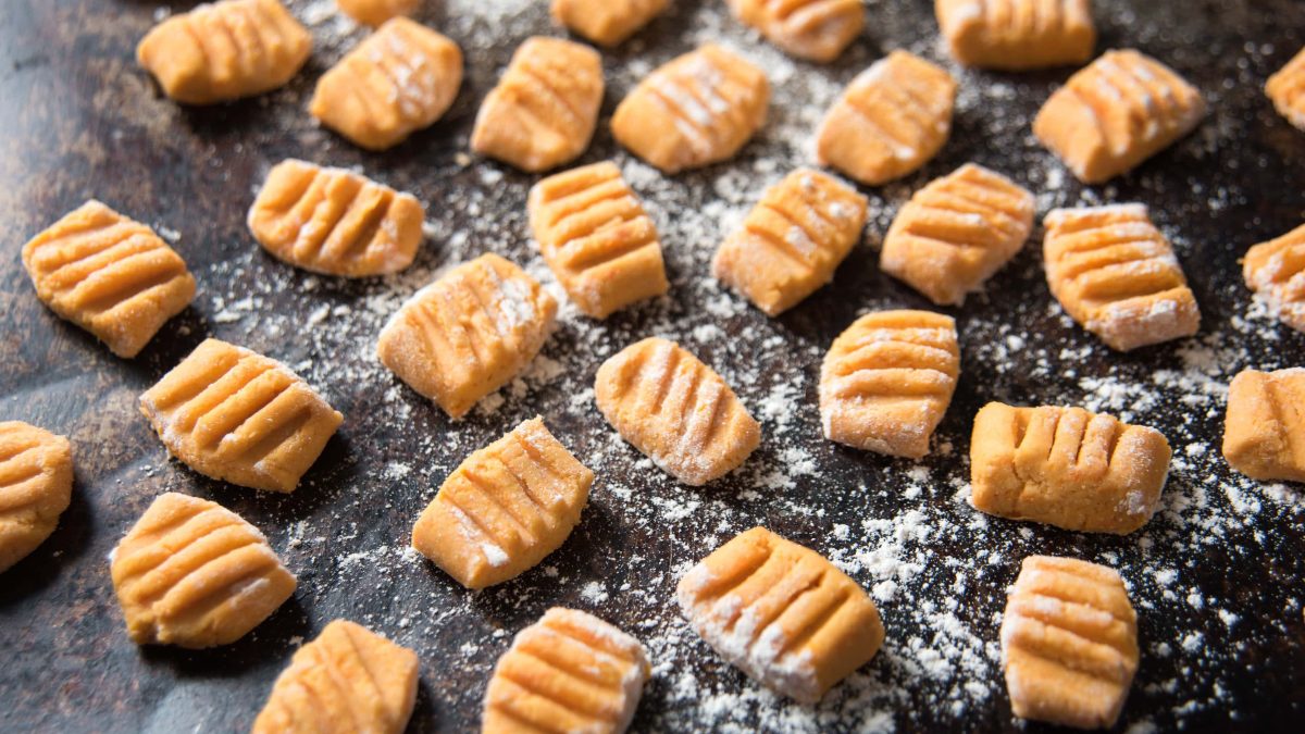 Süßkartoffel-Gnocchi mit Meh auf dunklem Untergrund.