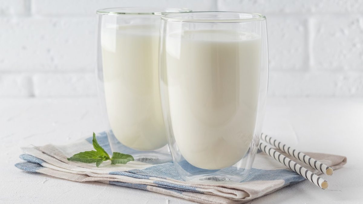 Vor einer weißen Wand stehen zwei Gläser, die mit dem türkischen Nationalgetränk Ayran gefüllt sind. Die Gläser stehen auf einem Handtuch.