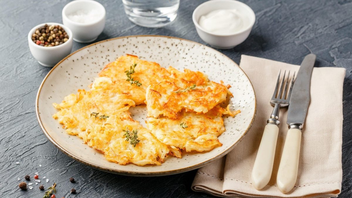 Vegane Kartoffelpuffer auf hellem Teller, mit Kräutern garniert, im Hintergund verschiedene Dips