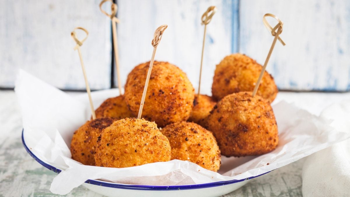 Ein Teller runde vegane Kroketten mit Spießen vor hellem Hintergrund.