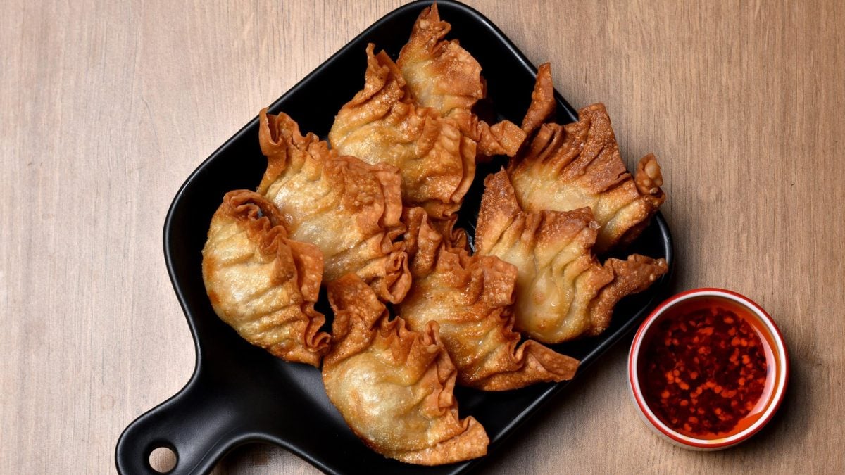 Frittierte vegane Wan Tans in einer schwarzen Pfanne, serviert mit scharfem roten Chili-Öl auf hölzernem Untergrund