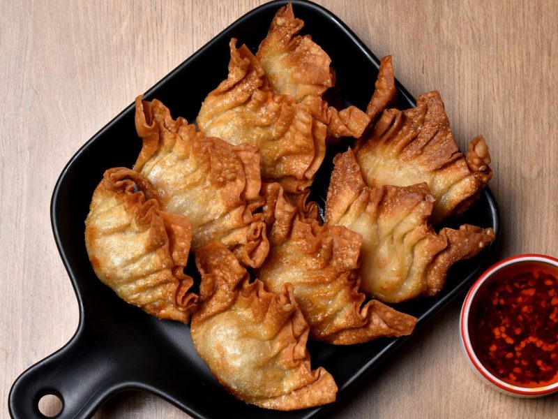 Frittierte vegane Wan Tans in einer schwarzen Pfanne, serviert mit scharfem roten Chili-Öl auf hölzernem Untergrund