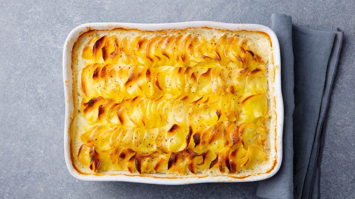 Eine weiße Auflaufform mit veganem Kartoffelgratin in der Draufsicht, daneben liegt eine Stoffserviette.