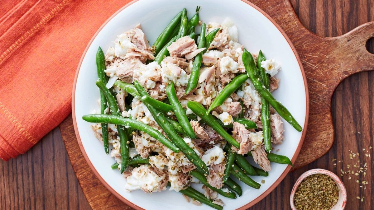Ein Teller voll Bohnen-Thunfisch-Salat steht auf einem Holzbrett auf einem Tisch.