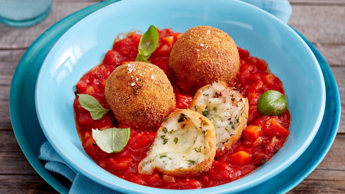 Arancini mit Tomatensugo auf einem blauen Teller. Das Ganze auf einem hölzernen Untergrund.