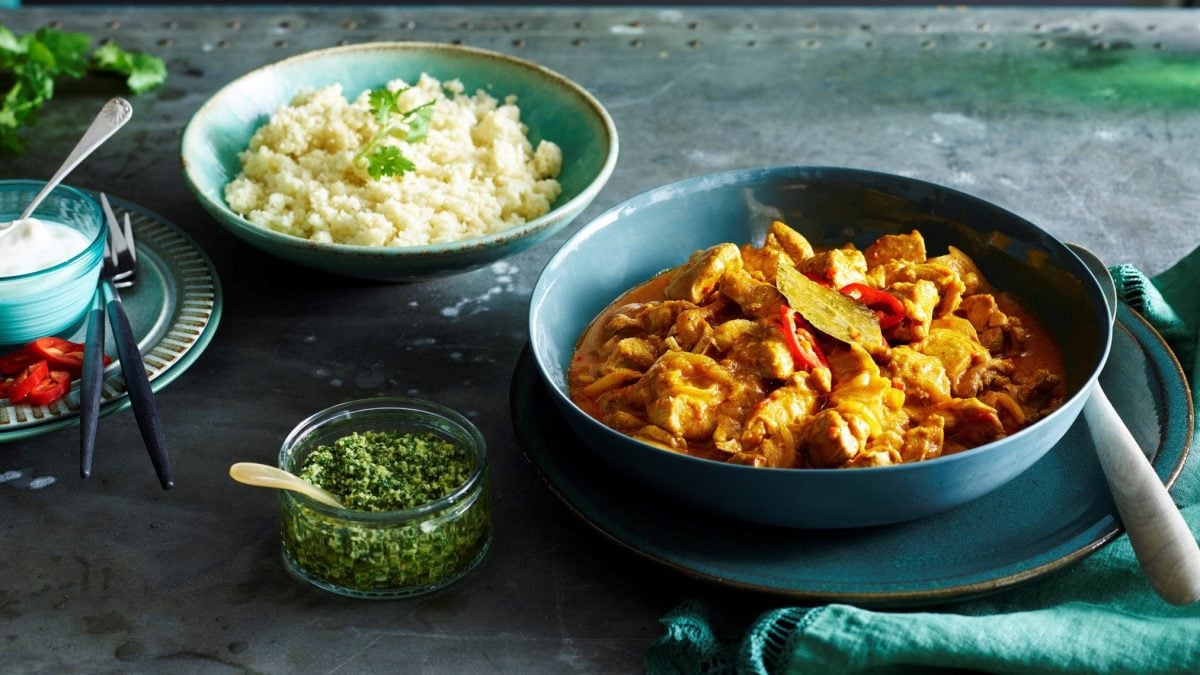 Blaue Schale gefüllt mit Chicken-Curry. Daneben befindet sich eine Schale Joghurt und eine weitere Schale Blumenkohlreis.