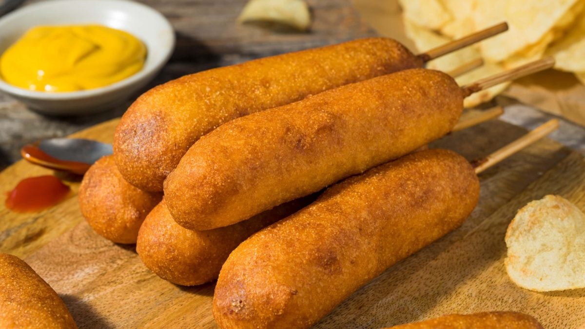 seitliche aufnahme von corn dogs mit senfschale im hintergrund auf holzbrett
