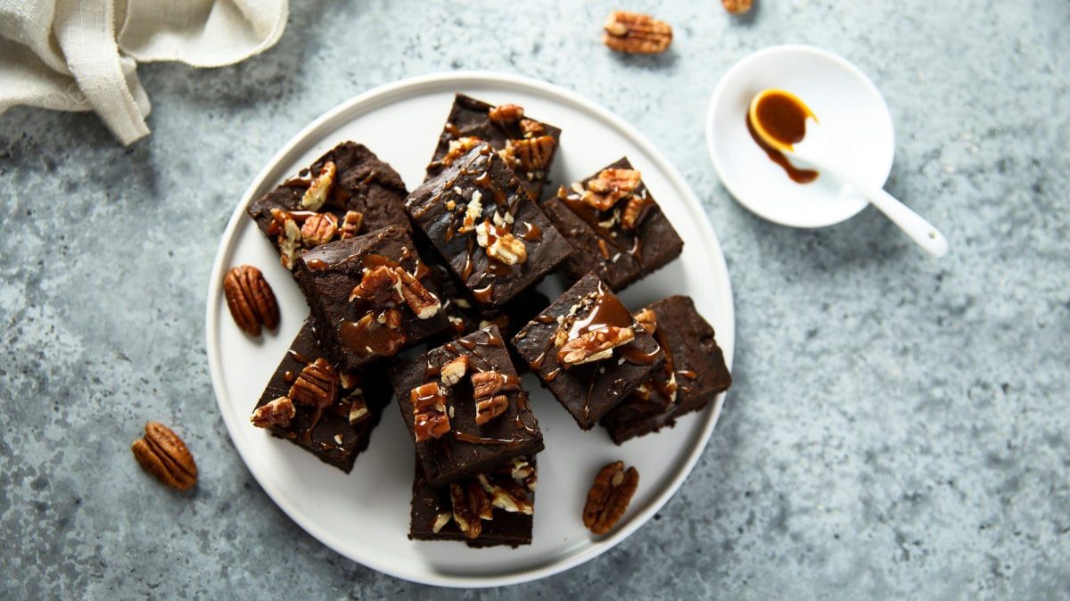 Auf einem weißen Teller liegen mehrere Stück Brownies mit Pekannüssen. Sie sind mit einem Klecks Schokoladensoße und Pekannüssen verziert.