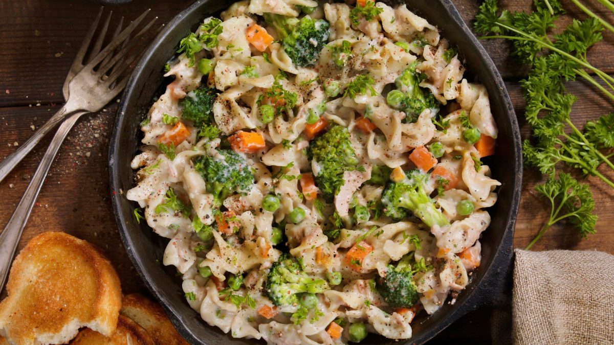 Pfanne mit Pasta, Thunfisch und Gemüse auf hölzernem Untergrund.