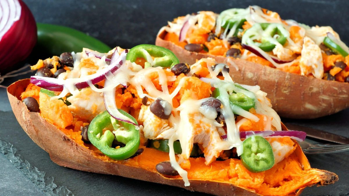 Zwei gefüllte Süßkartoffeln mit scharfem Gemüse und Chicken liegen auf einer Schieferplatte.