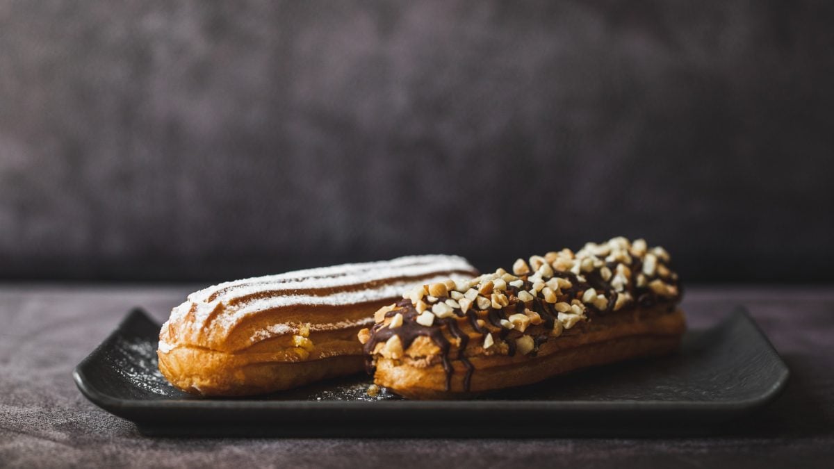 Zwei Eclairs von der Seite auf schwarzem Teller.