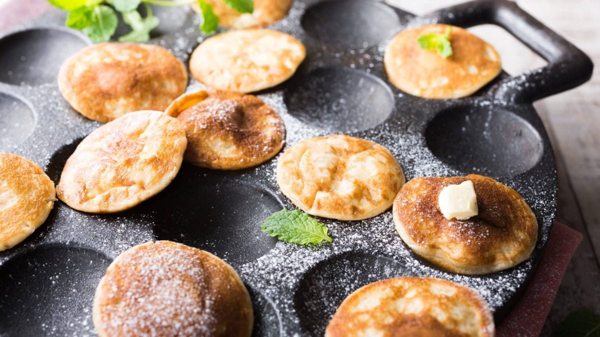 Die kleinen Poffertjes liegen mit Puderzucker bestäubt direkt in der speziellen Pfanne, in der sie gebacken wurden.