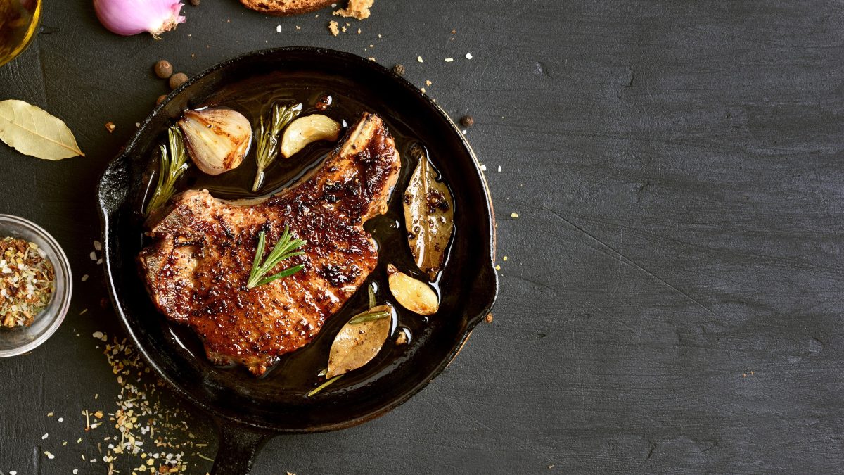 pfanne mit fleisch und gewürzen von oben auf schwarzem tisch
