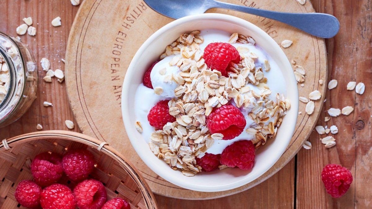 In einer Schüssel ist ein Haferflocken-Frucht-Quark angerichtet. Oben drauf sind frische Himbeeren.