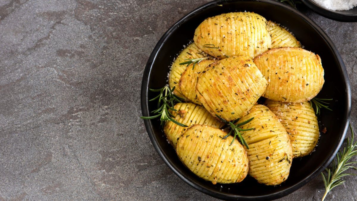 Hasselback-Kartoffeln mit Rosmarin auf schwarzem Teller.