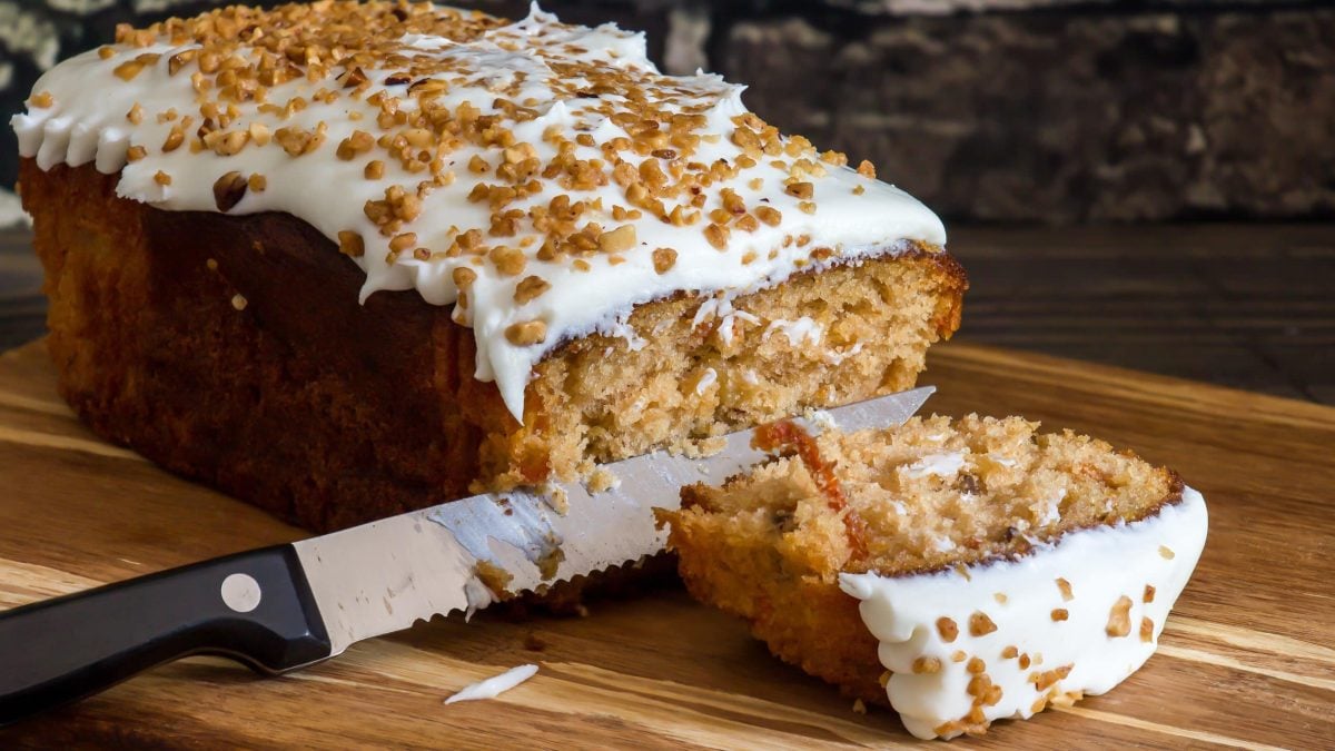 Karottenkuchen mit Frosting wird auf einem Holzbrett angeschnitten.