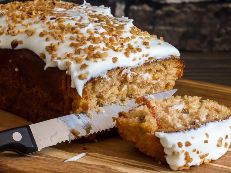 Karottenkuchen mit Frosting wird auf einem Holzbrett angeschnitten.
