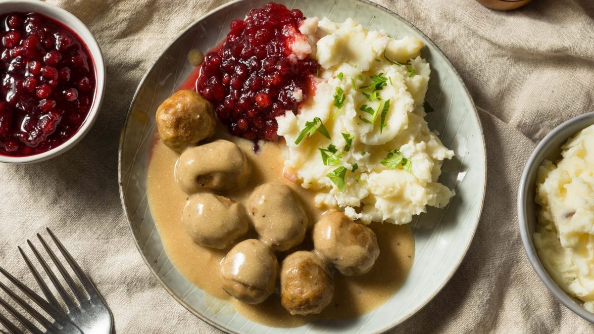 Köttbullar mit Soße, Preiselbeeren und Kartoffelpüree auf hellem Tischtuch.