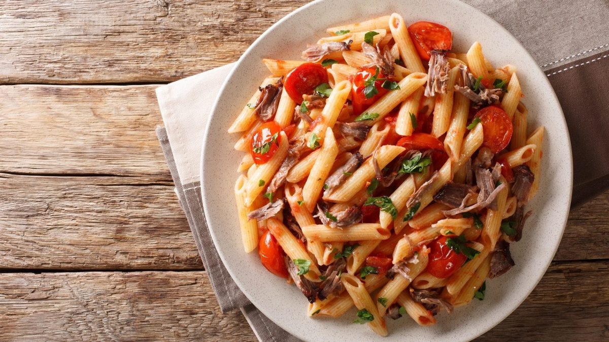 Ein prallgefüllter Teller mit unserer Pulled-Pork-Pasta steht auf einem Holztisch.