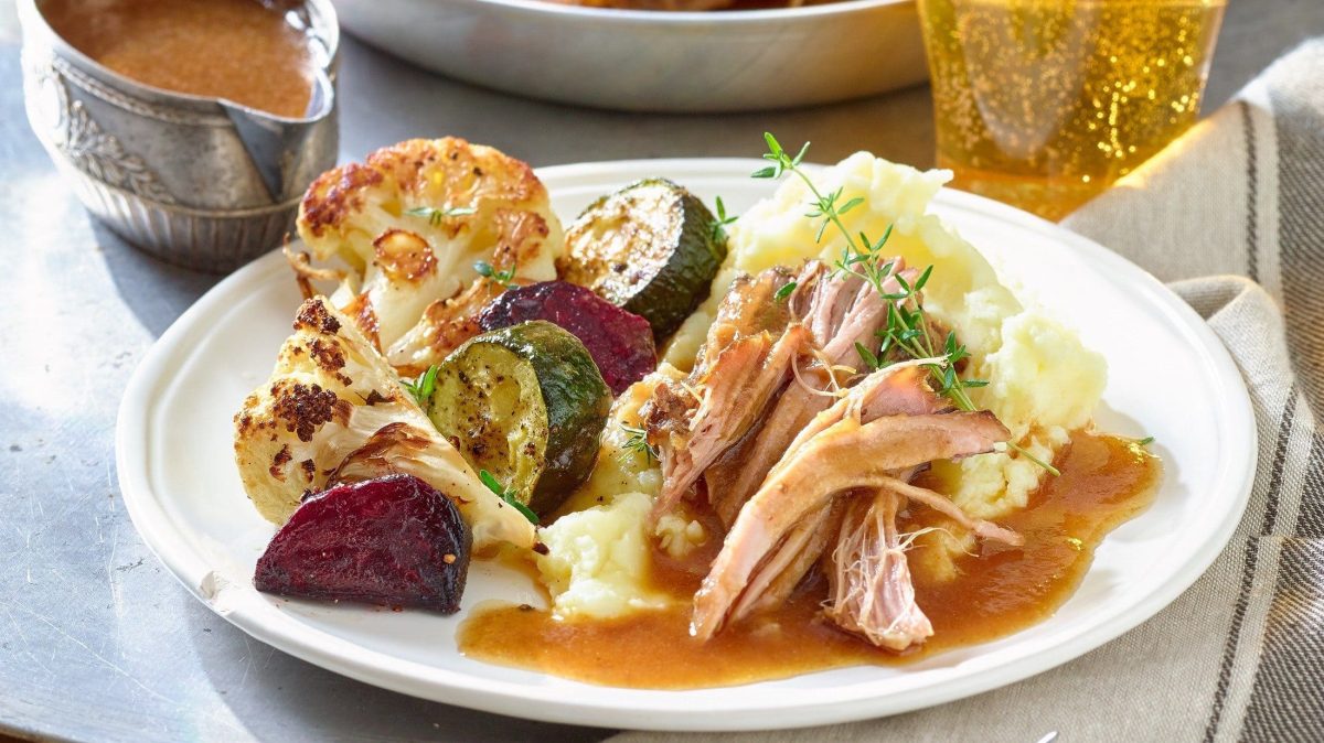 Ein Teller gefüllt mit Pulled-Pork-Sonntagsbraten steht auf dem Tisch. Dazu gibt es ein kühles Bier.